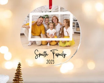 May include: A round, clear, acrylic Christmas ornament with a photo of a family of five inside a white frame. The text "Smith Family 2023" is printed below the photo.