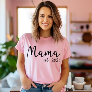 以下が含まれることがあります： 黒い文字で「ママ est. 2024」と書かれたピンクのTシャツ