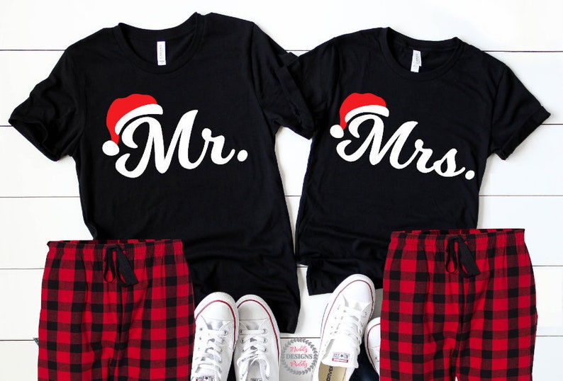 May include: A pair of black t-shirts with red Santa hats and the words "Mr." and "Mrs." printed on them. The shirts are paired with red and black checked pyjama bottoms.