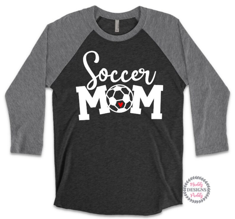 May include: A black and gray baseball tee shirt with a white soccer ball and the text "Soccer Mom" in white. The soccer ball has a small red heart in the center.