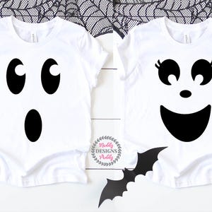 May include: Two white t-shirts with black ghost faces. One ghost has oval eyes and a vertical oval mouth. The other ghost has eyelashes, round eyes, and a smiling mouth. A black bat and the text "Muddy Designs Paddy" are also visible.