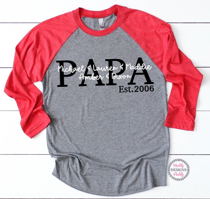 May include: A gray and red baseball tee shirt with the word "PAPA" in large black letters. The text "Michael & Lauren & Maddie Amber & Dixon Est. 2006" is written in white cursive letters below the word "PAPA".