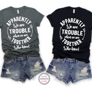 May include: Two gray and black t-shirts with white text that reads "Apparently We Are Trouble When We Are Together Who Knew!"