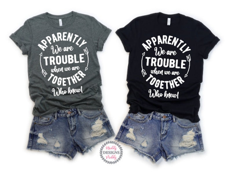 May include: Two gray and black t-shirts with white text that reads "Apparently We Are Trouble When We Are Together Who Knew!"