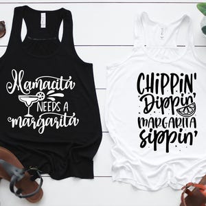 May include: Two white tank tops with black text. The top on the left says "Mamacita Needs a Margarita" with a margarita glass graphic. The top on the right says "Chippin' Dippin' Margarita Sippin'" with a lime graphic.