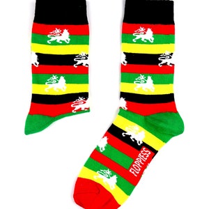 Peut inclure: Une paire de chaussettes colorées avec un motif rayé en rouge, vert, jaune et noir. Les chaussettes ont un motif de lion blanc sur chaque rayure. Les chaussettes sont étiquetées "FLOPPINESS".