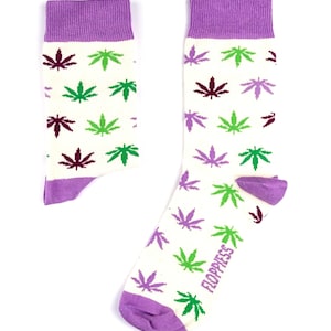 Peut inclure: Une paire de chaussettes blanches avec un revers violet et un motif de feuilles de marijuana vertes et violettes. Les chaussettes ont le mot "Floppiess" imprimé sur le côté.