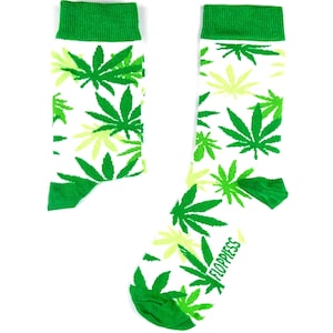 Peut inclure: Une paire de chaussettes blanches avec un motif de feuilles de marijuana vertes. Les chaussettes ont des revers verts et les mots "Floppiess" sont imprimés sur la chaussette droite.