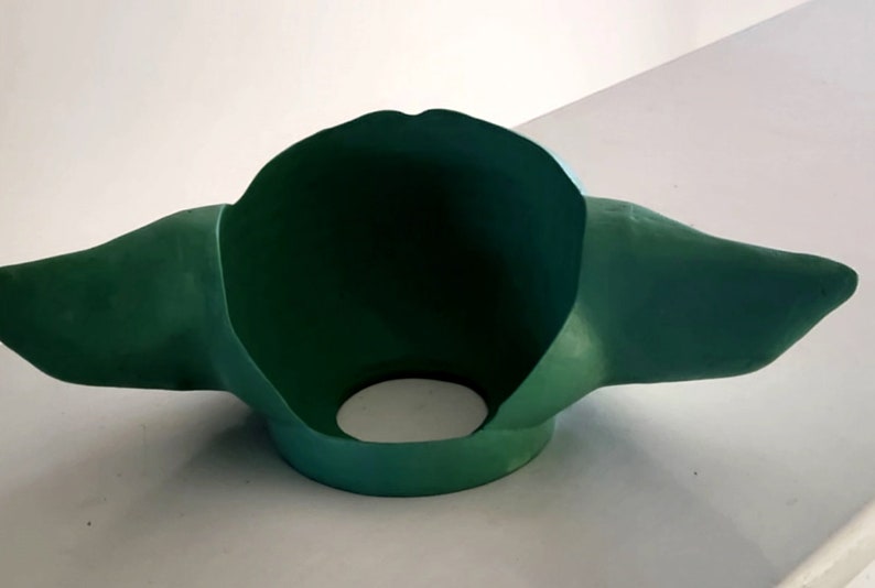 May include: Green felt Yoda mask with large ears. The mask is open at the front and has a hole in the bottom for the wearer's neck.