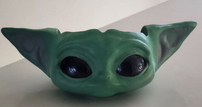 May include: Green ceramic planter shaped like a character from the Star Wars franchise, with large black eyes and two pointed ears.