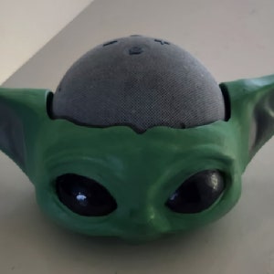 May include: A green and grey 3D printed figurine of a character from the Star Wars franchise. The figurine is designed to hold a small speaker.