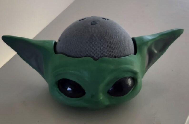 May include: A green and grey 3D printed figurine of a character from the Star Wars franchise. The figurine is designed to hold a small speaker.