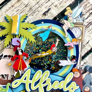 May include: A colorful cake topper featuring characters from Peter Pan, including Peter Pan, Captain Hook, Tinkerbell, and Wendy. The topper also includes a palm tree, a clock tower, and the name "Alfredo".