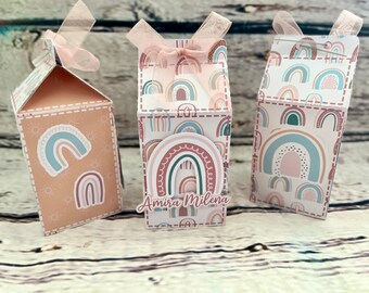 Könnte beinhalten: Drei kleine Milchpackungsförmige Schachteln mit Regenbogen-Designs. Die Schachteln sind mit pastellfarbenen Regenbögen verziert und haben einen hellbraunen Hintergrund. Die mittlere Schachtel trägt den Namen "Amira Milena".
