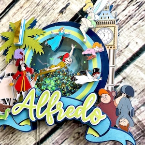 May include: A multi-layered cake topper featuring characters from Peter Pan and the Disney movie,  "Peter Pan." The topper includes Peter Pan, Captain Hook, Tinkerbell, Wendy, John, and Michael. The topper also includes a green palm tree, a blue and white striped banner with the name "Alfredo" on it, and a clock tower.