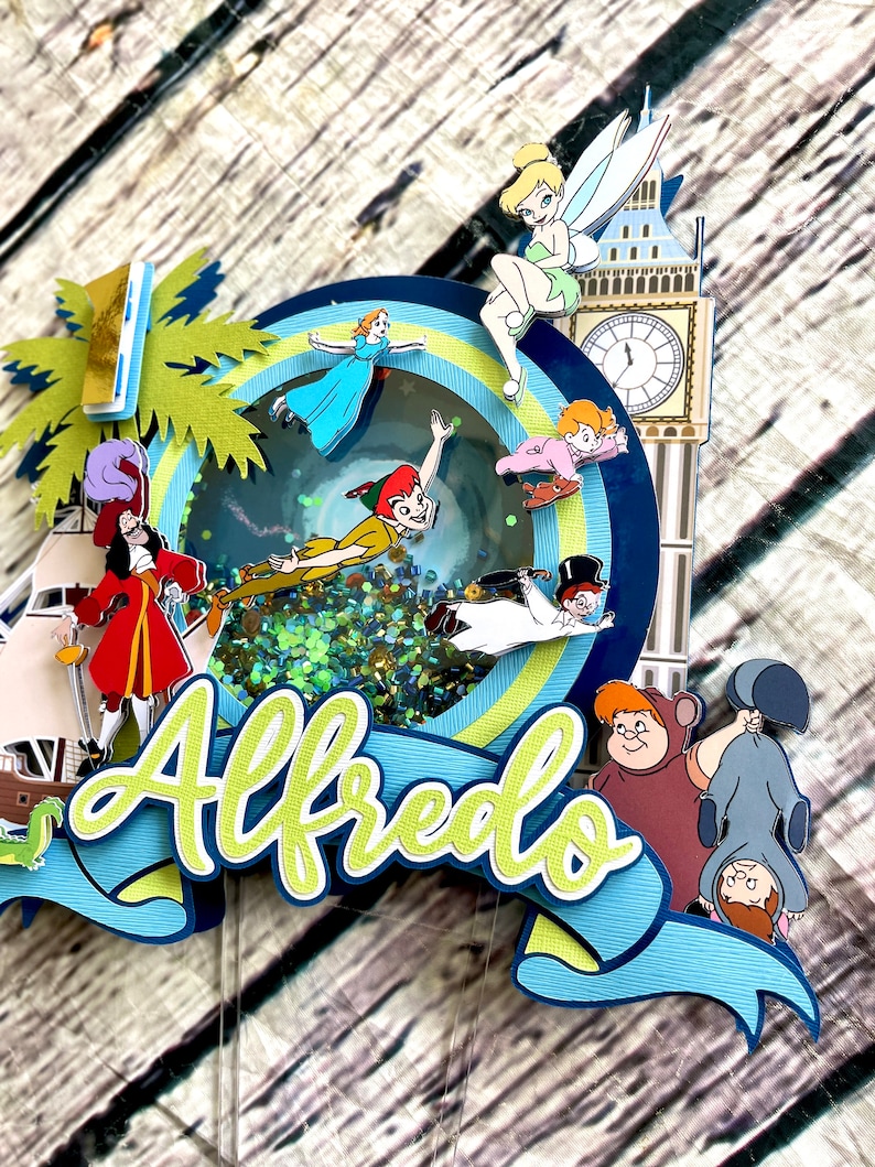May include: A multi-layered cake topper featuring characters from Peter Pan and the Disney movie,  "Peter Pan." The topper includes Peter Pan, Captain Hook, Tinkerbell, Wendy, John, and Michael. The topper also includes a green palm tree, a blue and white striped banner with the name "Alfredo" on it, and a clock tower.