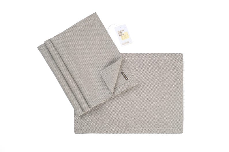 May include: Set of four gray linen placemats with a subtle texture. The placemats are folded and stacked, with a tag that reads "Easy to wash, easy to style" attached to the top.