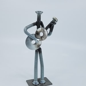 May include: A silver metal sculpture of a person playing a guitar made from screws and washers.