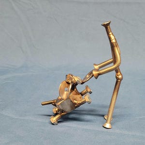 May include: A metal sculpture of a person holding a dog. The sculpture is made of screws and bolts and is painted silver.