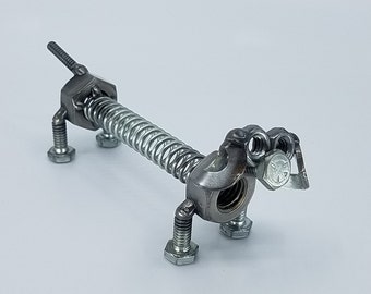 May include: A silver metal dachshund sculpture made from nuts, bolts, and a spring. The sculpture is a whimsical and unique piece of art.