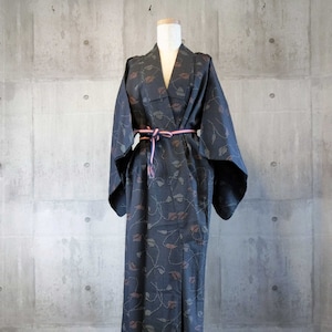 Puede incluir: Un kimono azul oscuro con un patrón floral. El kimono está atado con una faja rosa y negra.