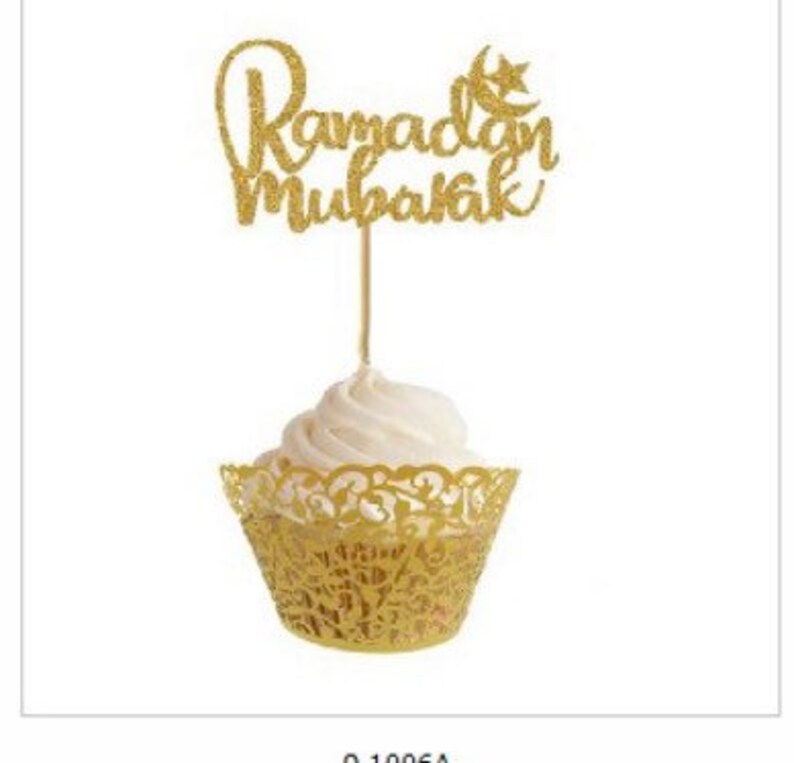 May include: Gold glitter cupcake topper with the text "Ramadan Mubarak" and a crescent moon and star. The topper is on top of a white cupcake with a gold lace cupcake wrapper.