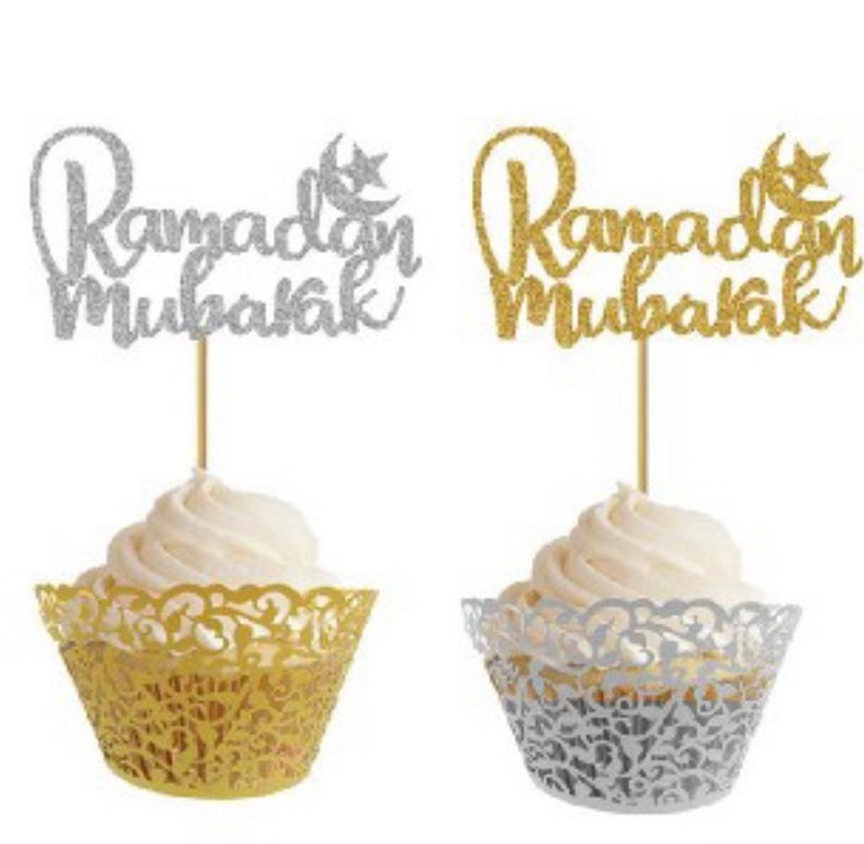 May include: Two cupcake toppers with the words "Ramadan Mubarak" in silver glitter and gold glitter. The toppers are on top of cupcakes with gold and silver cupcake liners.