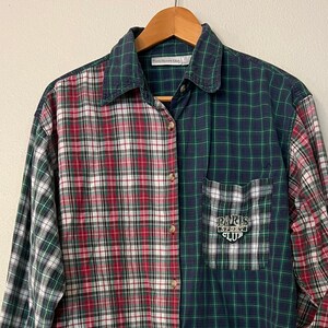 May include: A long-sleeved plaid button-up shirt with a red, white, and green plaid on the left side and a blue and green plaid on the right side. The shirt has a pocket on the right side with a "Paris" logo.