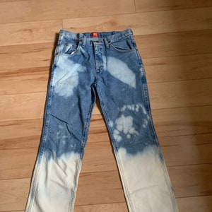 May include: A pair of blue denim jeans with a bleached effect. The jeans are faded at the bottom and have a white, bleached pattern throughout.
