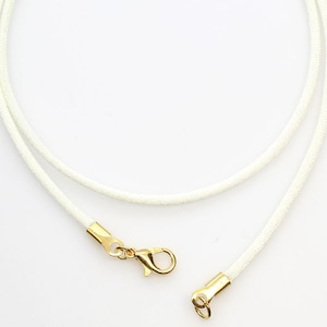 May include: A white cord necklace with gold-toned lobster clasp and jump ring.