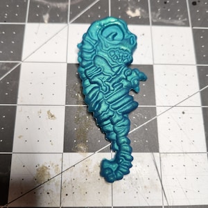 May include: A teal blue seahorse figurine with a detailed, textured design. The seahorse is standing upright with its tail curled.