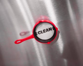 Puede incluir: Una sartén roja y negra con un círculo blanco en el centro que dice "CLEAN" en letras negras.