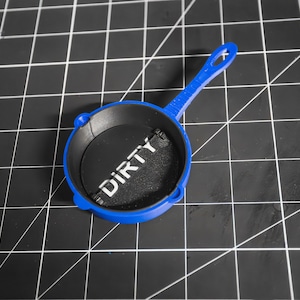 May include: A blue toy frying pan with a black interior and the word "DIRTY" printed in white on the interior.