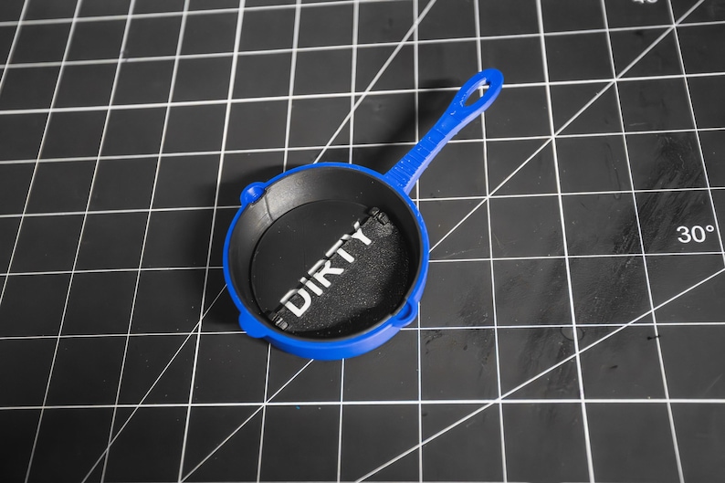 May include: A blue toy frying pan with a black interior and the word "DIRTY" printed in white on the interior.
