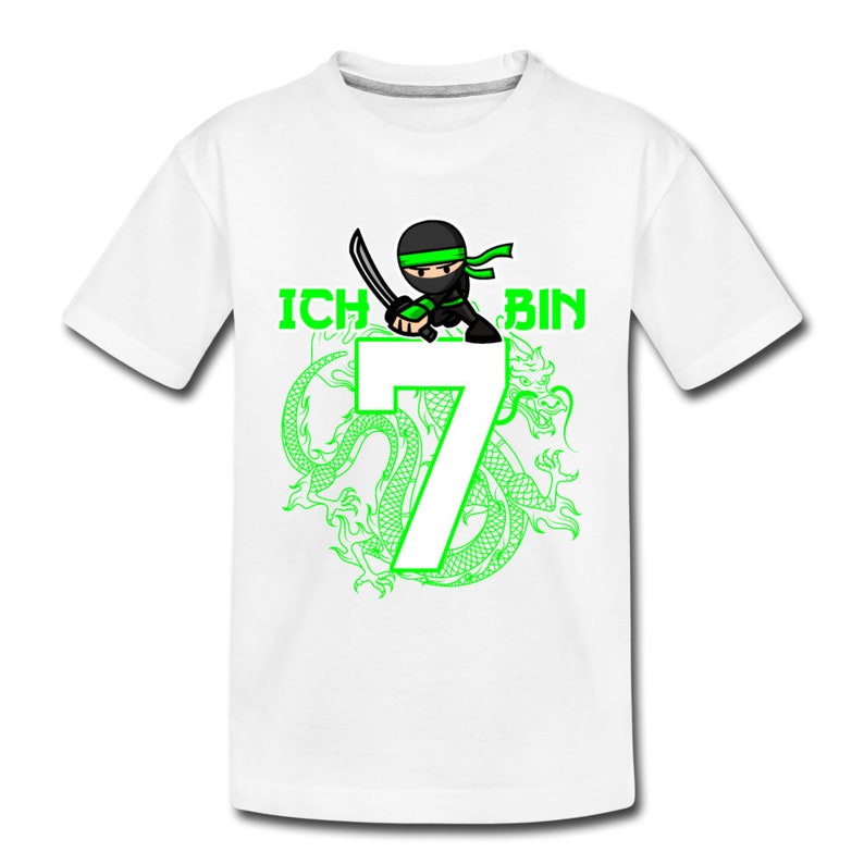 Op de afbeelding: Wit T-shirt met een groene ninja-cartoon die een zwaard vasthoudt en op het nummer 7 staat. De tekst "ICH BIN" staat boven het nummer. Het nummer 7 is omringd door een groene draak.