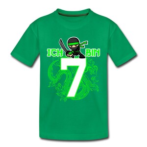 Op de afbeelding: Groen T-shirt met een groene ninja-cartoon die een zwaard vasthoudt en de tekst "ICH BIN 7" in groene letters. De ninja staat op een groene draak.