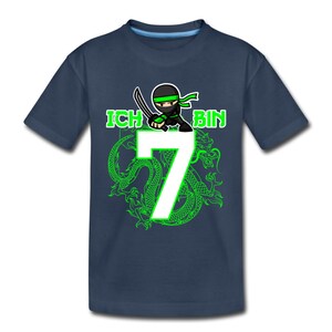 Op de afbeelding: Een donkerblauw T-shirt met een groene ninja-cartoon die een zwaard vasthoudt en een groen drakenontwerp. De tekst "ICH BIN 7" is op het shirt gedrukt.