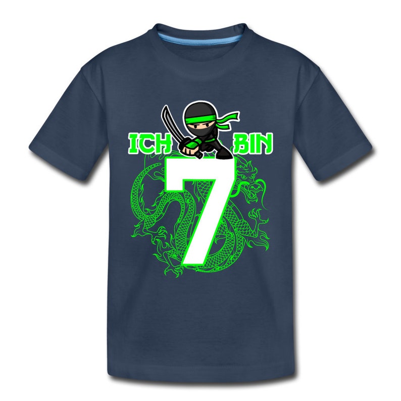Op de afbeelding: Een donkerblauw T-shirt met een groene ninja-cartoon die een zwaard vasthoudt en een groen drakenontwerp. De tekst "ICH BIN 7" is op het shirt gedrukt.