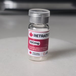 Peut inclure: Un petit flacon en verre transparent avec un bouchon en métal argenté et une étiquette blanche et rose. L'étiquette présente une icône de feuille d'érable rouge, le texte RETRATUT, 100mg, LYOPHILIZED POWDER FOR RESEARCH ONLY, PROUDLY CANADIAN.