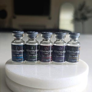Peut inclure: Cinq flacons en verre transparent avec des bouchons gris, chacun étiqueté RETATRUTIDE 10MG 99% PURITY RESEARCH GRADE COMPOUND FOR RESEARCH ONLY. Les étiquettes présentent des bordures colorées distinctes en bleu, vert, rouge, violet et jaune.