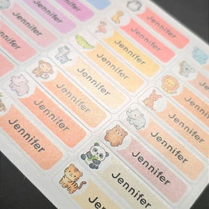 May include: A sheet of rectangular adhesive labels featuring the name Jennifer printed in black text. Each label includes a small, colourful cartoon animal illustration, such as a tiger, panda, bear, monkey, or lion, set against pastel backgrounds.
