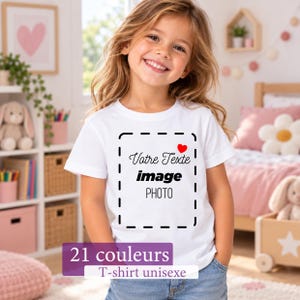 Peut inclure: Un t-shirt blanc à manches courtes avec un cadre rectangulaire en pointillés noirs, une petite icône de cœur rouge au-dessus du texte "Votre Texte", "image" et "PHOTO". Le t-shirt présente un bandeau violet avec "21 couleurs" et "T-shirt unisexe".