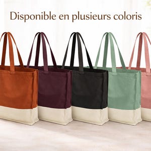 May include: Five canvas tote bags in shades of rust, burgundy, black, sage green, and dusty rose. Each bag features a contrasting off-white base and matching handles. The French text "Disponible en plusieurs coloris" is visible at the top.