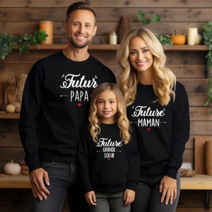 Peut inclure: Une famille de trois personnes portant des sweat-shirts noirs avec du texte blanc. Le sweat-shirt du père dit "Futur Papa" avec une flèche et un cœur. Le sweat-shirt de la mère dit "Future Maman" avec une flèche et un cœur. Le sweat-shirt de l'enfant dit "Future Grande Soeur" avec une flèche et un cœur.