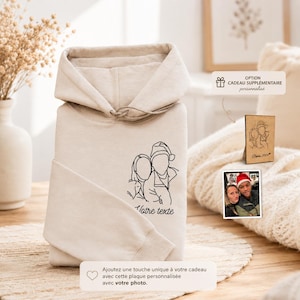 Peut inclure: Un sweat à capuche beige avec un dessin au trait noir de deux personnes et le texte "Votre texte". L'image comprend également une petite plaque en bois avec un portrait de couple et une photo d'un couple. Le sweat à capuche a une capuche à cordon.