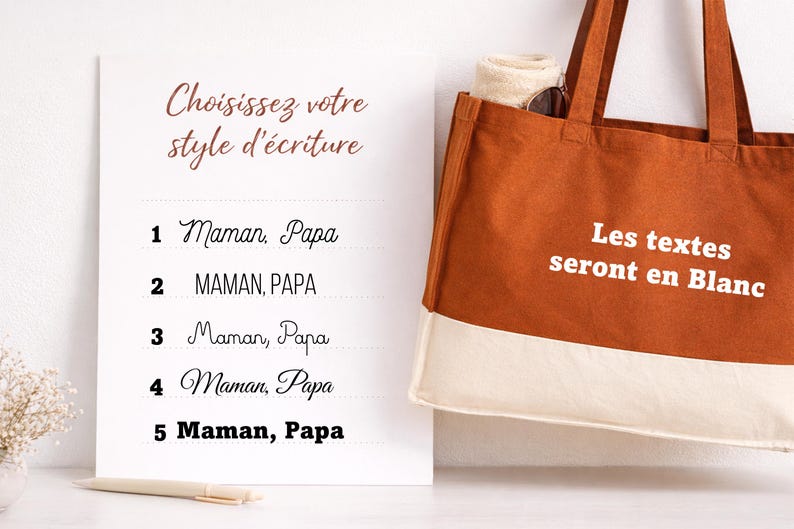 May include: A white sign with French text, beside a brown tote bag. The sign shows font choices for text, including "Maman, Papa." The tote bag has white text that reads "Les textes seront en Blanc."