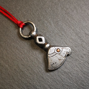 May include: A silver pendant necklace with a detailed animal head design. The pendant is attached to a red cord.