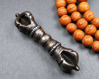 May include: A silver metal hand-shaped object with a brown wooden handle. The object is lying on a gray surface next to a string of brown beads.