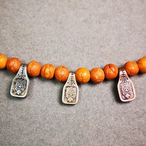 May include: A necklace made of orange beads with three silver pendants featuring a face design.