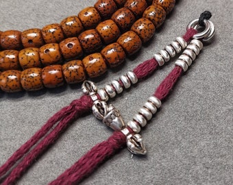 May include: A brown wooden mala bead necklace with a silver tassel and a red cord. The mala beads are strung on a cord and have a knotted tassel at the end.
